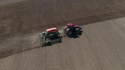 Red tractor pulling seed drill on field - pan right Stock Footage 313250383