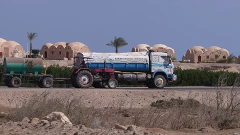 Red tractor pulling water tanker driving in marsa alam, egypt Video stock 333565490