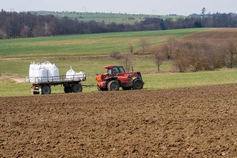 Red tractor pulls heavy sacks across tilled field, March 24, 2026, Velká Biteš Stock Photos