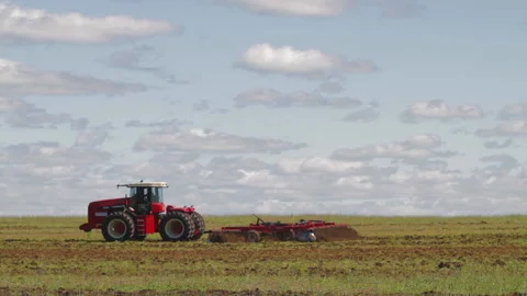 Red tractor with a reverse plow plows a field. A stork walks nearby and collects 스톡 동영상 150806278
