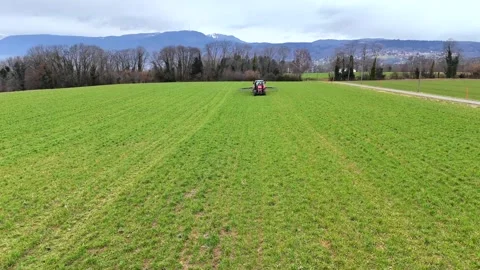 A red tractor is seen working in a vast green field in rural Switzerland. In the Stock Footage 330616075