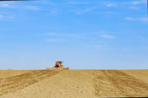 Red tractor sows grain with a seeder on a field in hilly terrain. Stock Photos
