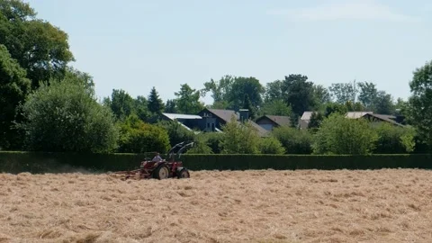 Red tractor turns cut dry grass into hay in Germany. Agricultural work Stock Footage 240183112