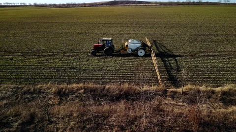 Red tractor with white sprayer attachment moves across green agricultural field 库存影片 332894450