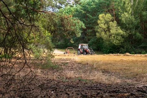 Red Tractor Working in a Field Surrounded by Forest in Poland Stock Photos