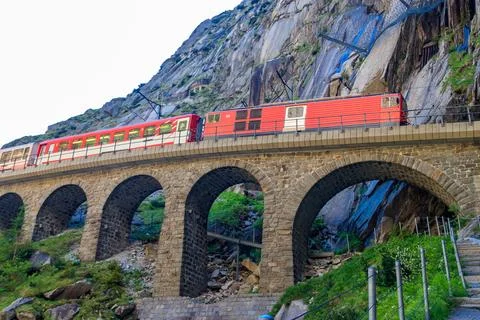 Red train passing by Devil's bridge at St. Gotthard pass on the Swiss Alps Stock Photos