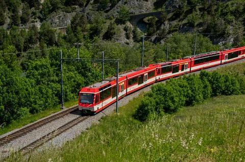 The red train passing on the rail in spring in Switzerland. Stock Photos