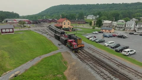A red train pulls into the station as people walk in the parking lot. The sunny Stock-Footage 331700301