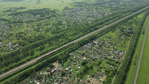 Red train speeding through lush green countryside, passing farmhouses, crop Stock Footage 316228797