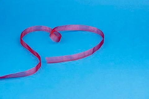 Red translucent ribbon in the shape of a heart on a blue background. Stock Photos