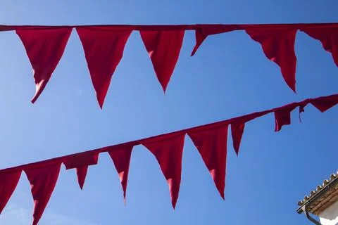 Red triangular bunting flags strung across a bright blue sky during a sunny d Stock Photos