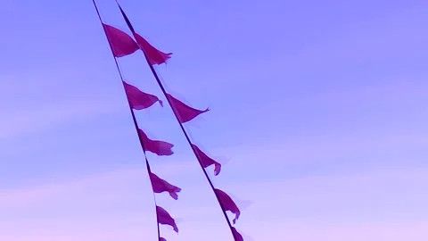 Red triangular flags flutter in the strong wind against a bright pink sky, Stock Footage 310558920