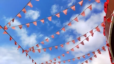 Red triangular flags flutter in the wind against a bright blue sky 動画素材 306636551