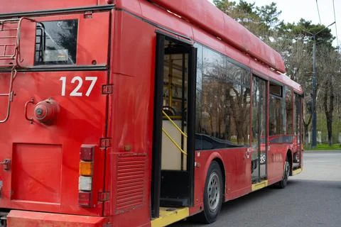 Red trolleybus number 127 parked at a stop on a sunny day surrounded by trees Stock Photos