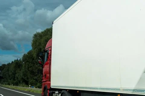 Red truck cab pulling a plain white box trailer along a highway shoulder, blank Stock Photos