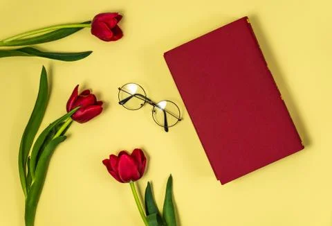 Red tulips with red book and glasses on yellow background , flat lay top view	 Stock Photos