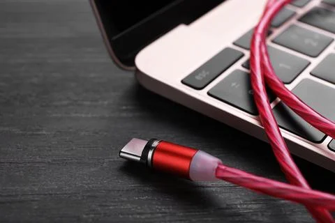 Red USB cable with type C connector and laptop on black wooden table, closeup Fotos Stock