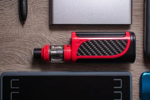Red vaping device flat on a table surrounded by technology Stock Photos