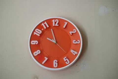 Red wall clock showing time at 11:55 in a room Stock Photos