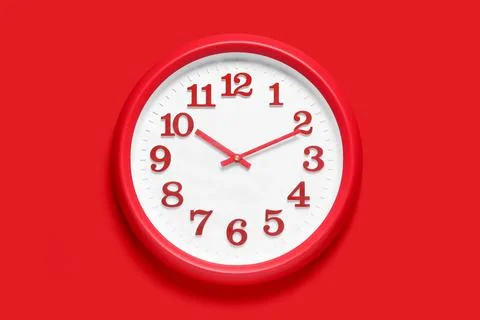 Red wall clock with white face and red numbers on a solid red background, tim Stock Photos