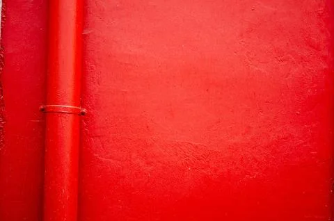 Red wall with vertical pipe, vibrant architectural background texture Stock Photos