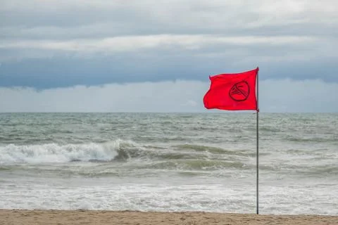 Red Warning Flag on a Cloudy Beach Foto stock