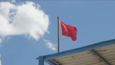 Red warning flag flapping in the wind over blue sky. Swimming is dangerous in Stock Footage 154596388