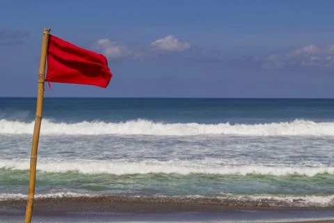 Red warning flag flapping in the wind on beach at stormy weather. Stock Photos