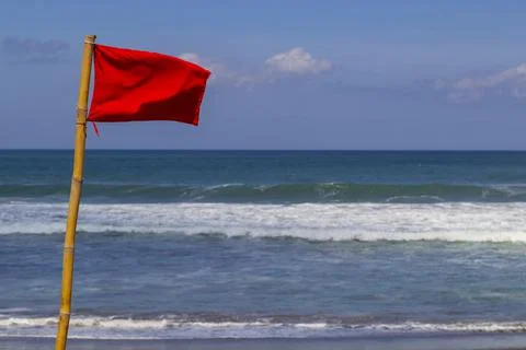 Red warning flag flapping in the wind on beach at stormy weather. Stock Photos