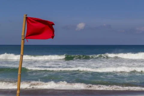 Red warning flag flapping in the wind on beach at stormy weather. Stock Photos