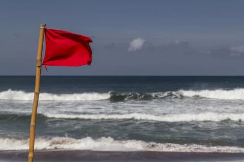 Red warning flag flapping in the wind on beach at stormy weather. Stock Photos