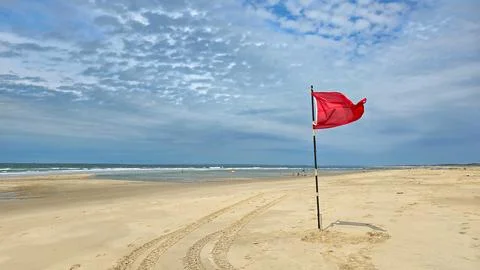 The red warning flag flies in the wind on a wide clean sandy beach of the Stock Photos