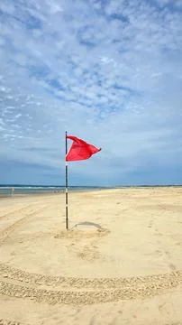 The red warning flag flies in the wind on a wide clean sandy beach of the Stock Photos