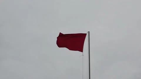 Red warning flag fluttering in slow motion against a gray cloudy sky Stock Footage 139875587