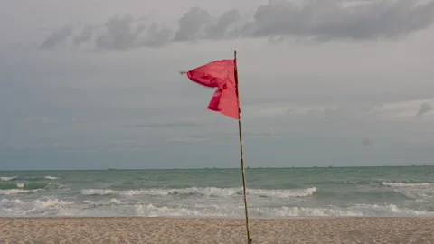 Red warning flag flutters rapidly in strong seaside wind above  beach 스톡 동영상 329214926
