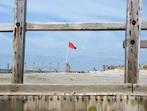 Red Warning Flag Flying on the Beach Framed by Weathered Wooden Groynes Stock Photos