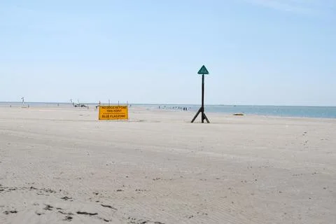 Red Warning Flag Flying on the Beach and View of Distant Coastal Defenses Stock Photos