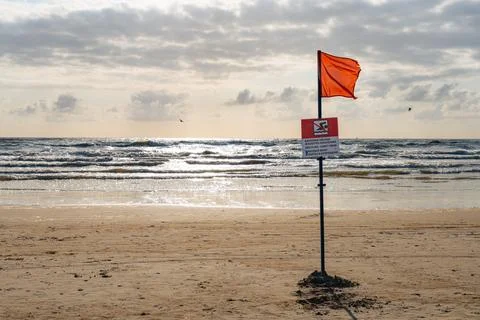 Red warning flag on a sandy beach. Danger sign at the ocean shore indicatin.. Фото