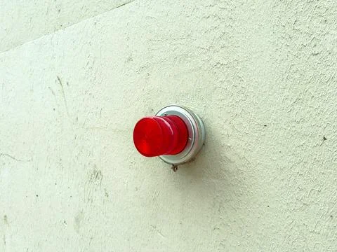 Red warning light fixed on a white wall in an industrial area during daytime Stock Photos