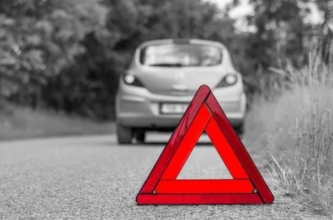 Red warning triangle and green broken car on the road - black and white conce Stock Photos