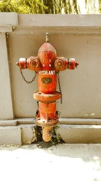 A red weathered fire hydrant mounted on a concrete sidewalk Stock Photos