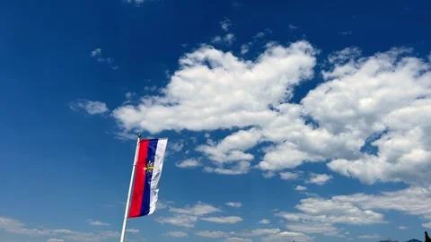 A red , white and blue flag is flying in the wind against a blue sky with clouds Stock-Footage 287079671