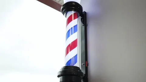 A red, white, and blue spinning Barber Shop sign in the window. Stock Footage 280356937