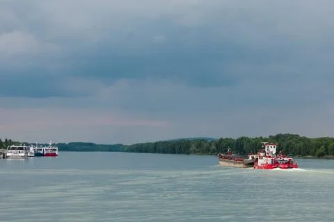 Red, white cargo ship sails along the wide part of River in cloudy weather, p Stock Photos