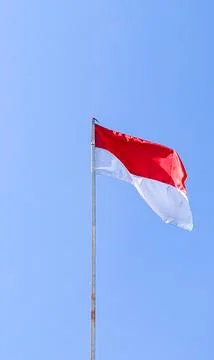 Red white Indonesian flag flutter on sturdy flagpole against clear blue sky.. Stock Photos