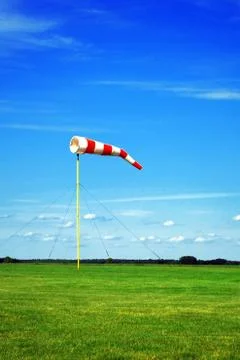 Red-white wind cone/sock/sleeve on a background of the blue cloudy sky and green Stock Photos