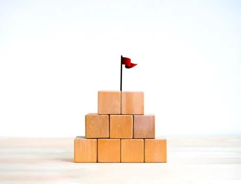 Red win flag on top of 5 wood blocks pyramid stack isolated on wooden table.. 스톡 사진