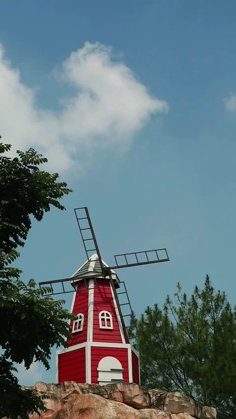 Red windmill standing on a rocky outcrop under a blue sky Stock Footage 333508763