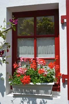 The red window is decorated with pots of geranium in France Stock Photos