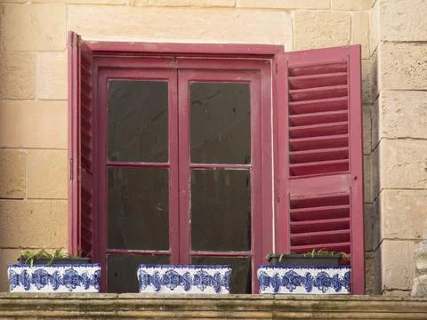 Red window with shutters and flower pots on a stone wall, the town of mdina on Fotos de archivo